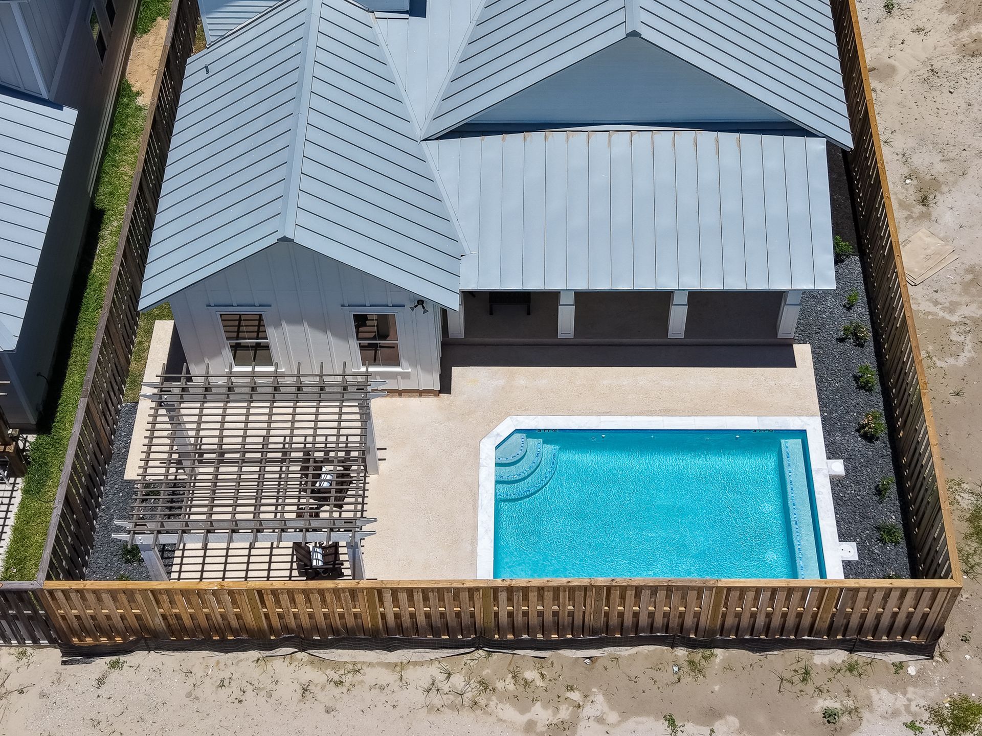 Aerial view of a fenced backyard with a swimming pool, patio, and house roof.