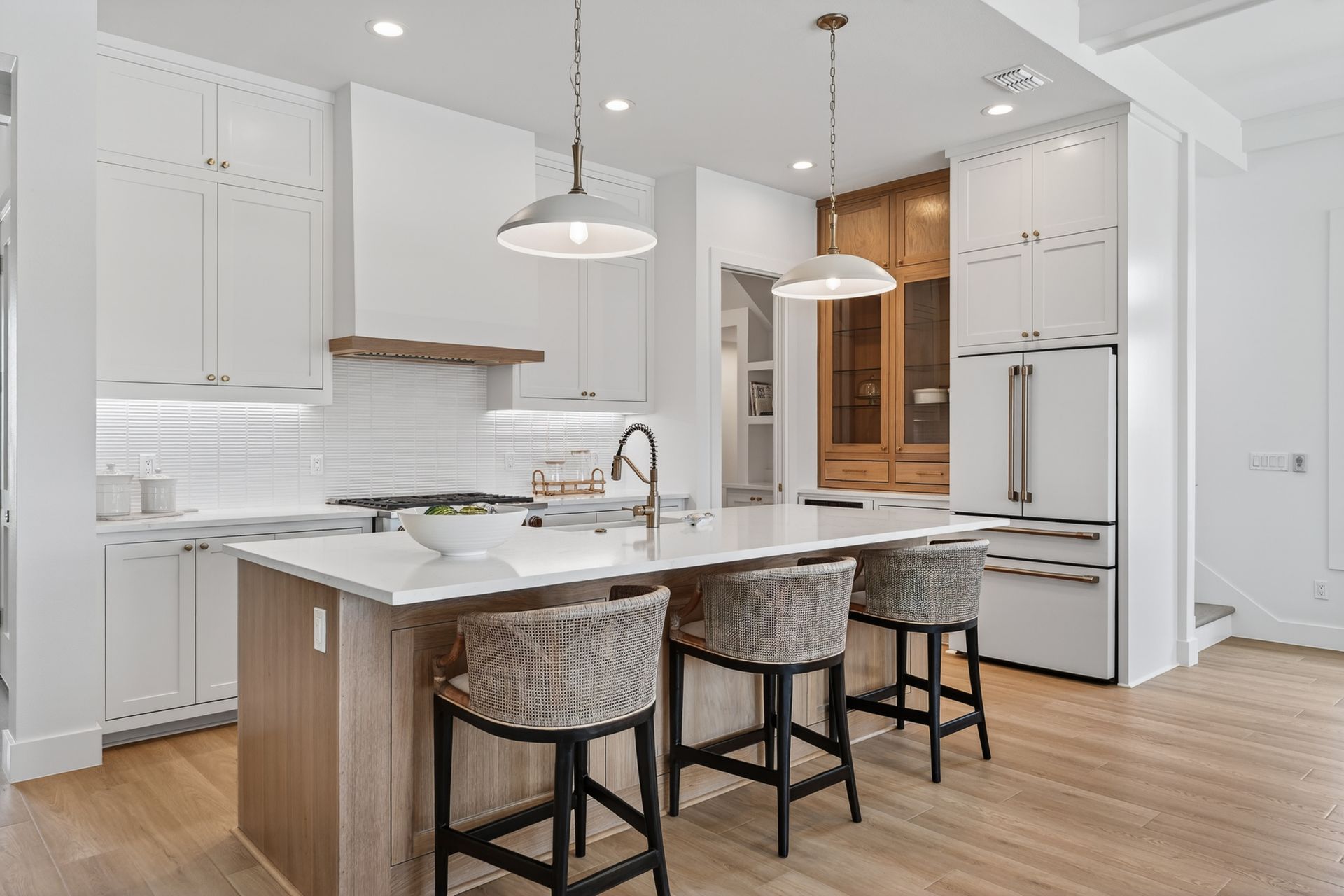 Bright modern kitchen with white cabinets, marble island, pendant lights, and bar stools