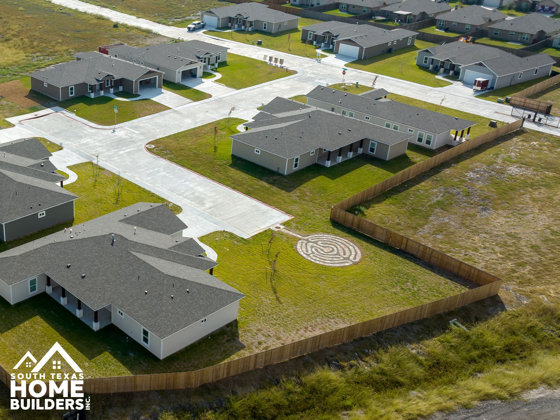 Aerial view of new homes in a suburban development with gray roofs, grass, and a wooden fence.
