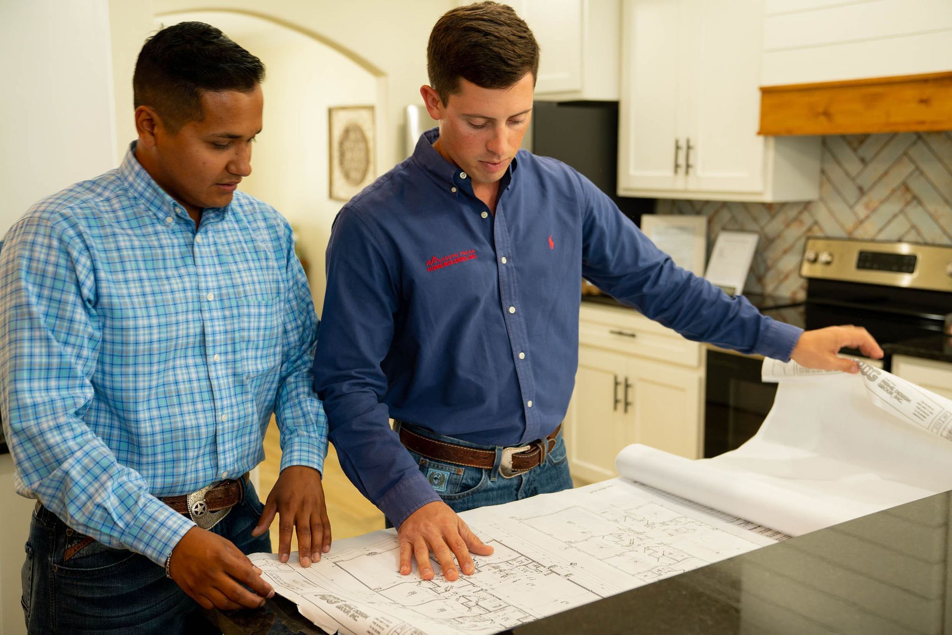 Two men are looking at a blueprint in a kitchen.