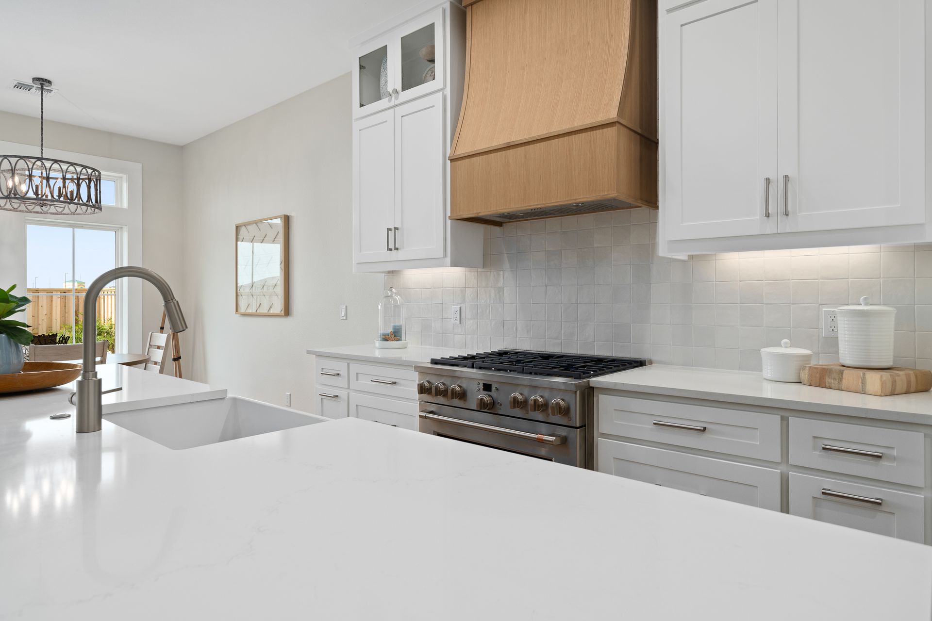 A kitchen with white cabinets , a stove , a sink , and a hood.