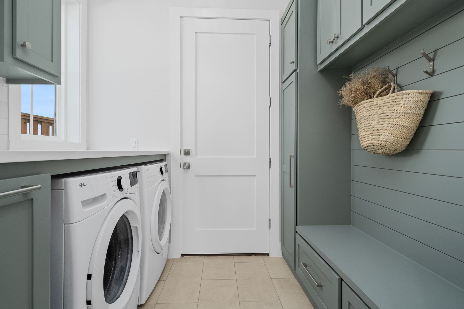 A laundry room with a washer and dryer and a basket hanging on the wall.