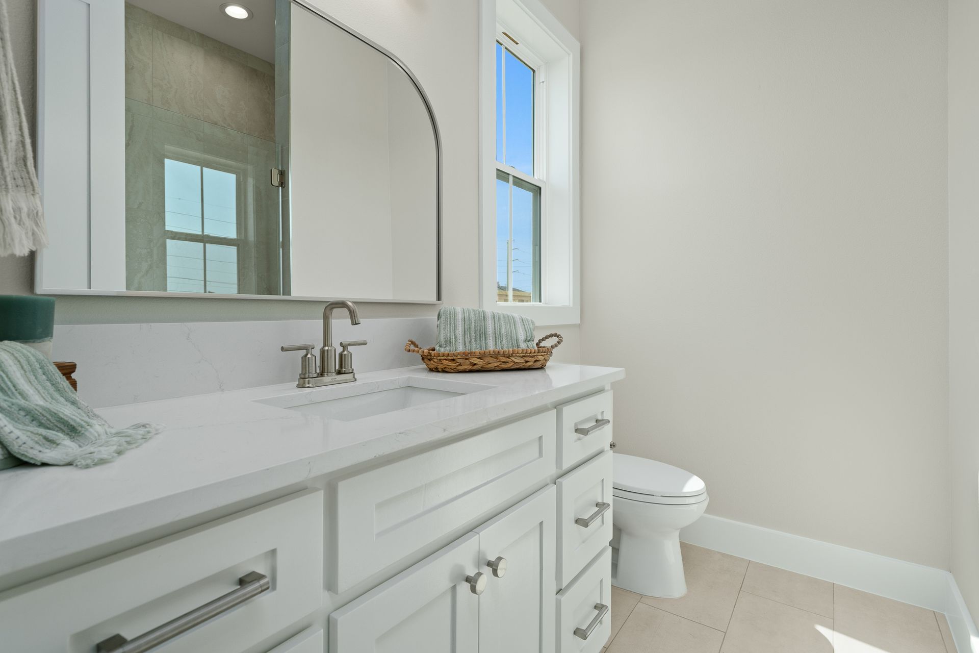 A bathroom with a sink , toilet , mirror and window.