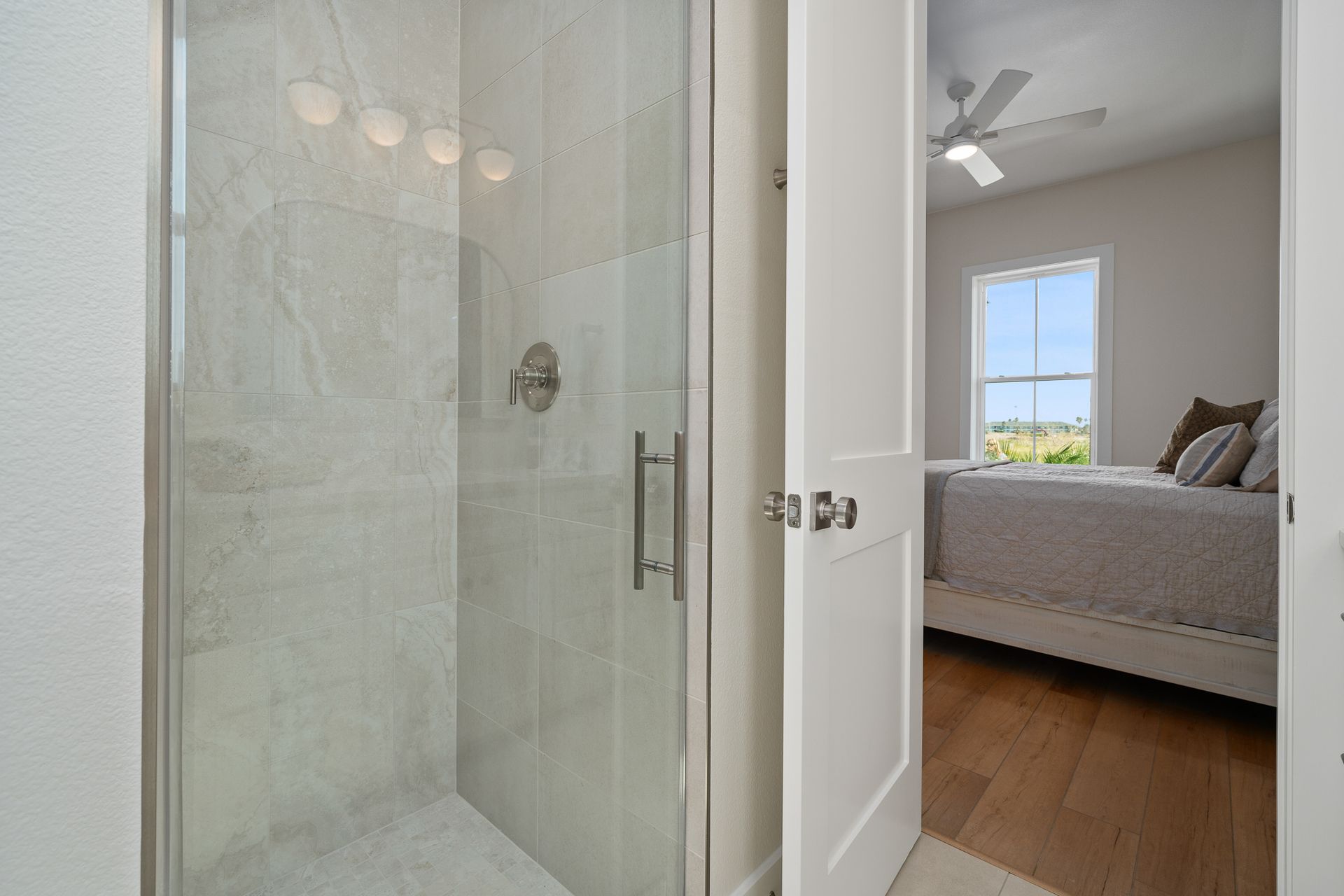 A bathroom with a walk in shower and a bedroom with a bed.