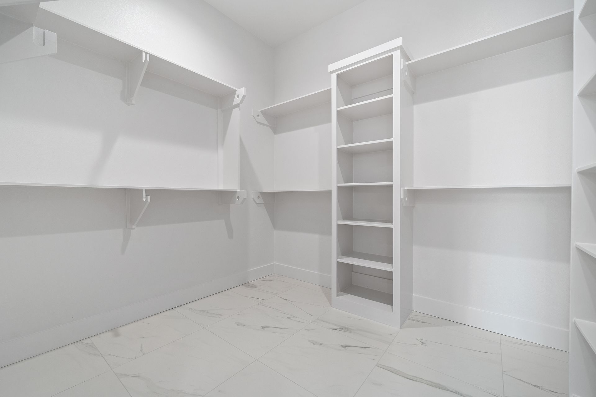 An empty walk in closet with white shelves and a white floor.