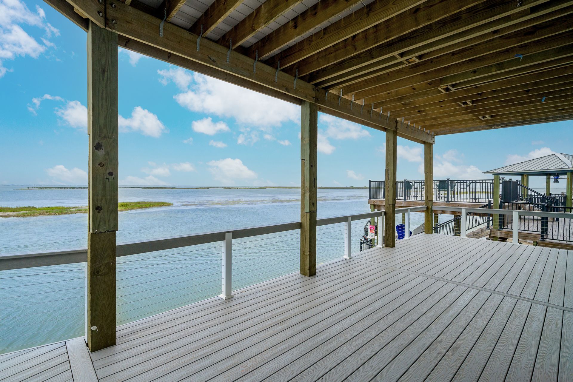 Wooden deck overlooking water, under a covered porch with a distant gazebo.