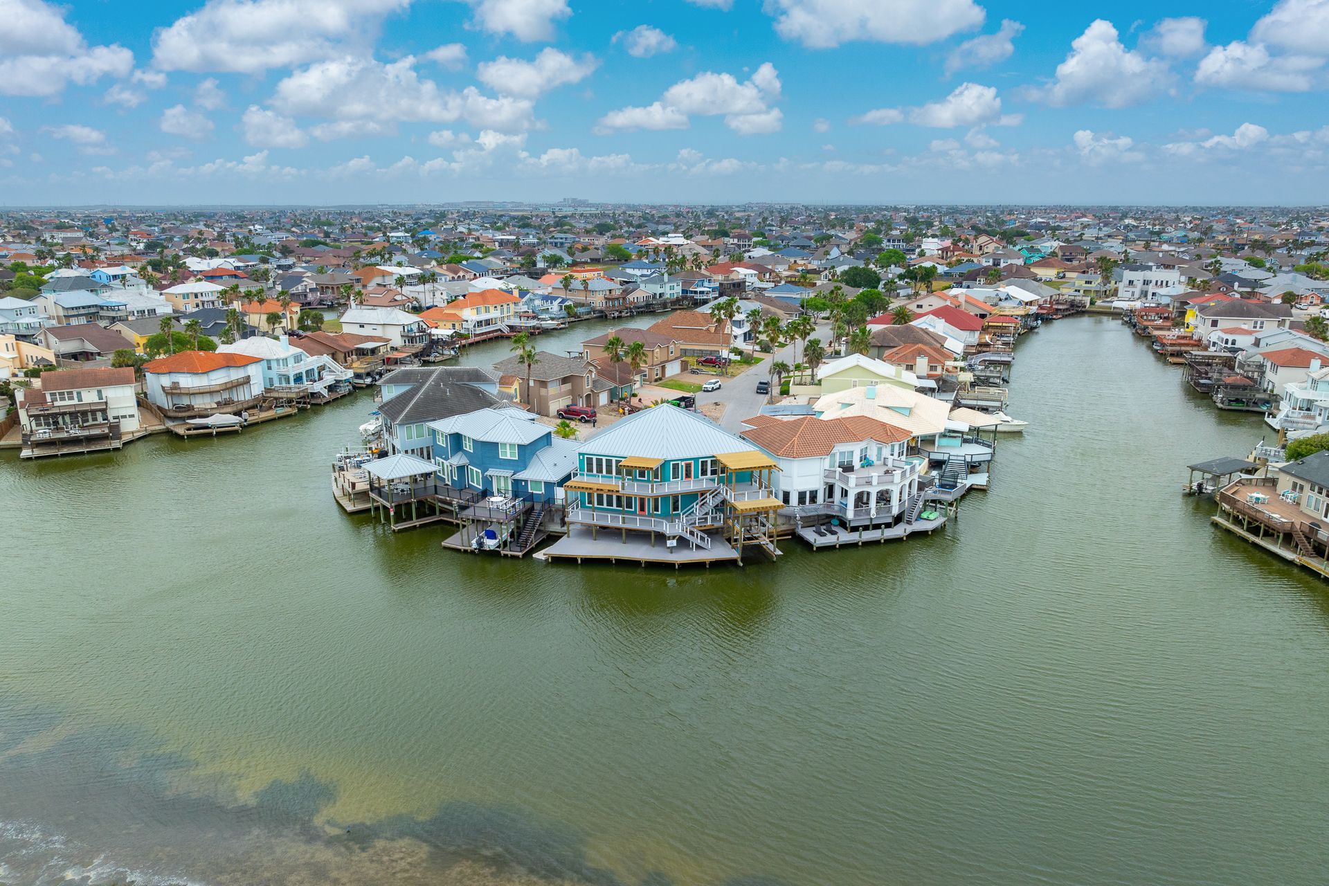 Aerial view of waterfront houses with boats on canals under a blue sky.