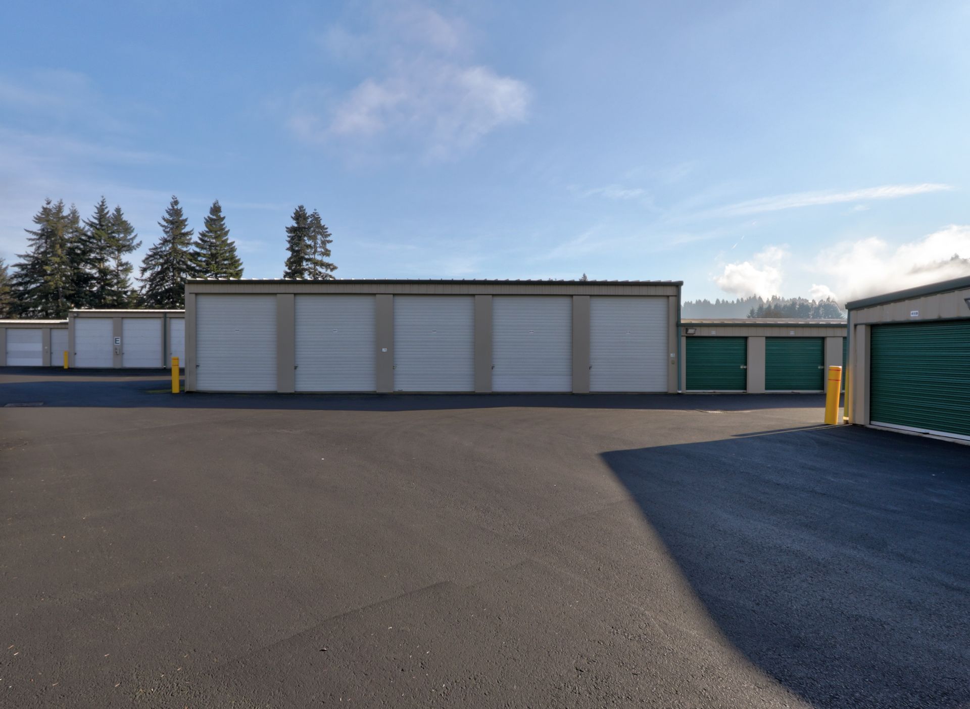 Storage units with gray doors and asphalt parking lot under a blue sky.