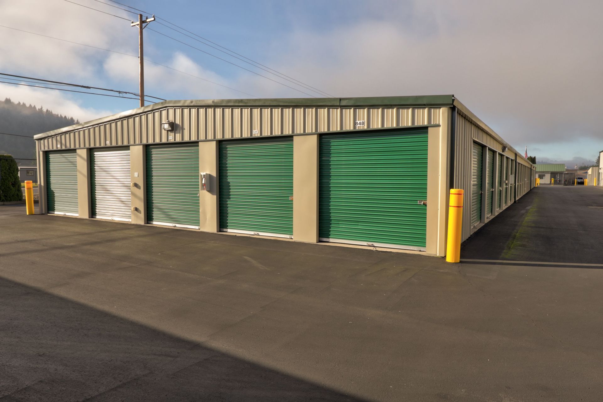 Storage units with green doors and a blacktop parking area.