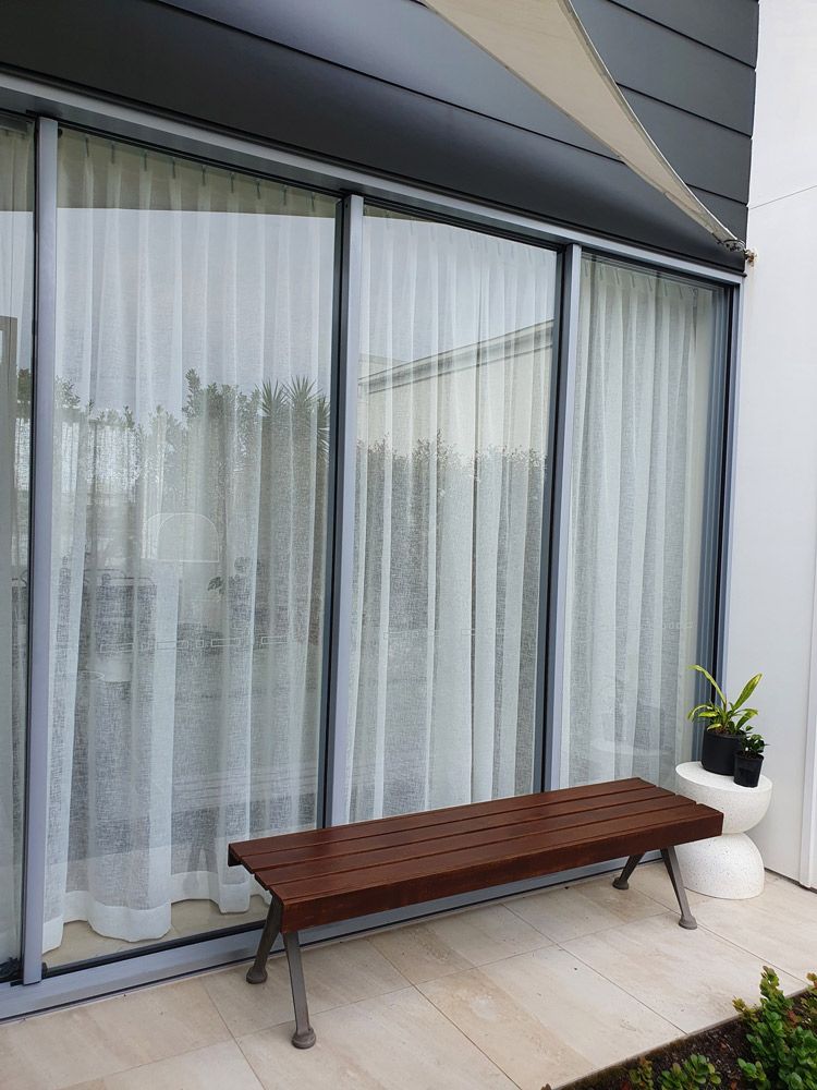 A Wooden Bench is Sitting in Front of a Large Window — Artizen Curtains in Mooloolaba, QLD