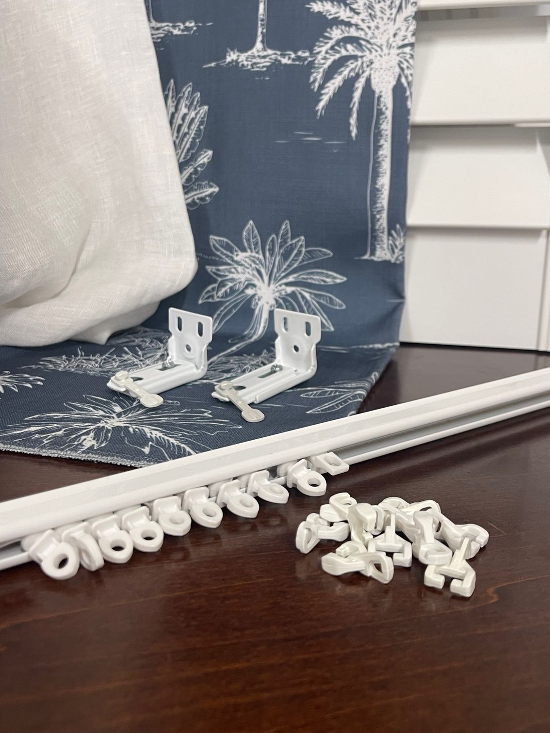 A White Curtain Rod is Sitting on a Wooden Table Next to a Blue Curtain — Artizen Curtains in Mooloolaba, QLD