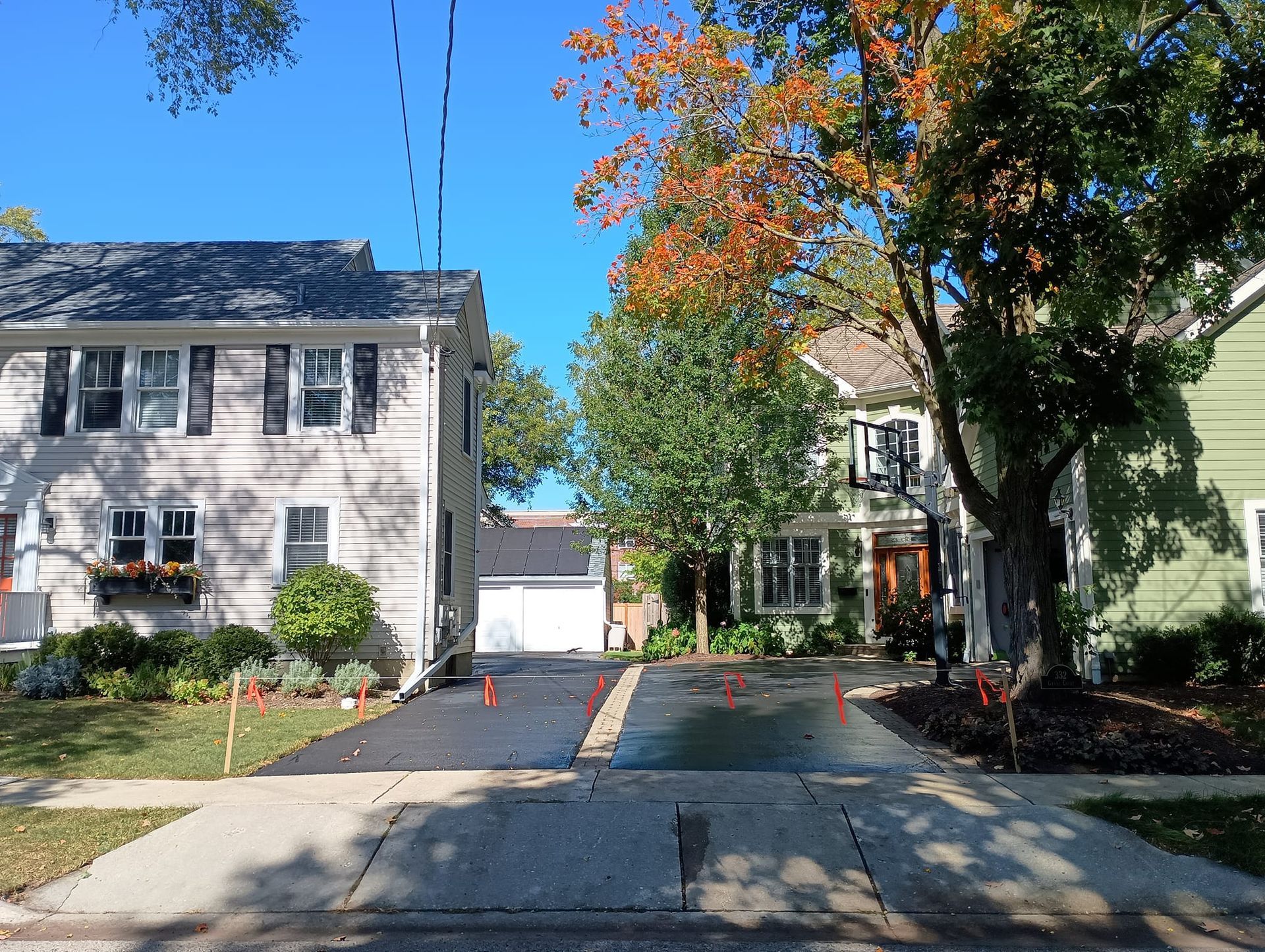 Residential street scene with newly paved driveways; autumn foliage and houses in the background.