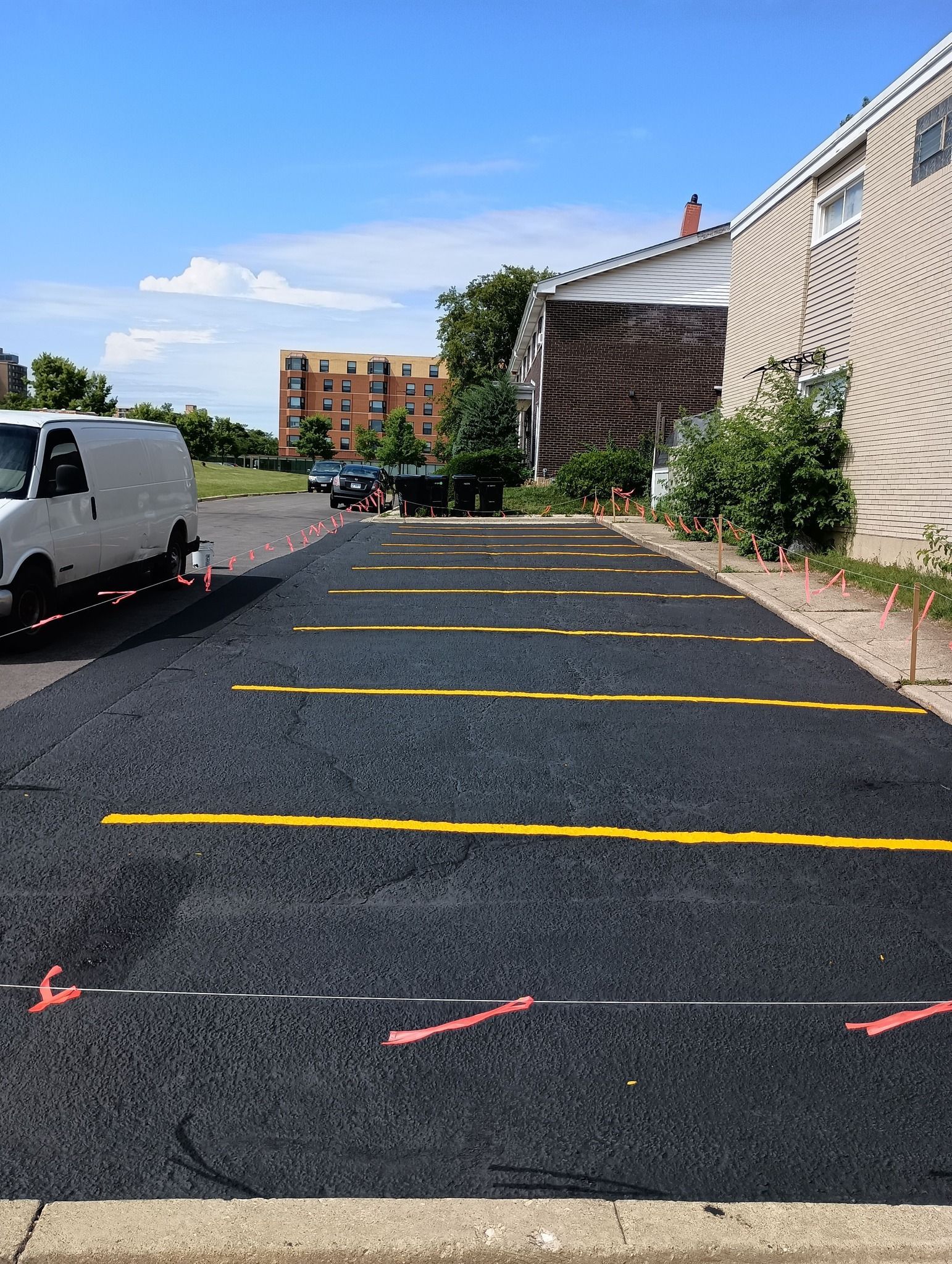 Newly paved parking lot with yellow lines and a white van on the left, building on the right, blue sky.