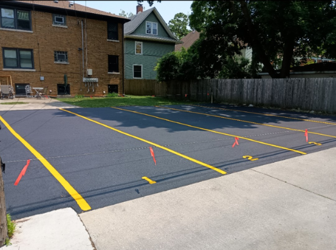 Newly paved parking lot with yellow lines and a white van on the left, building on the right, blue sky.