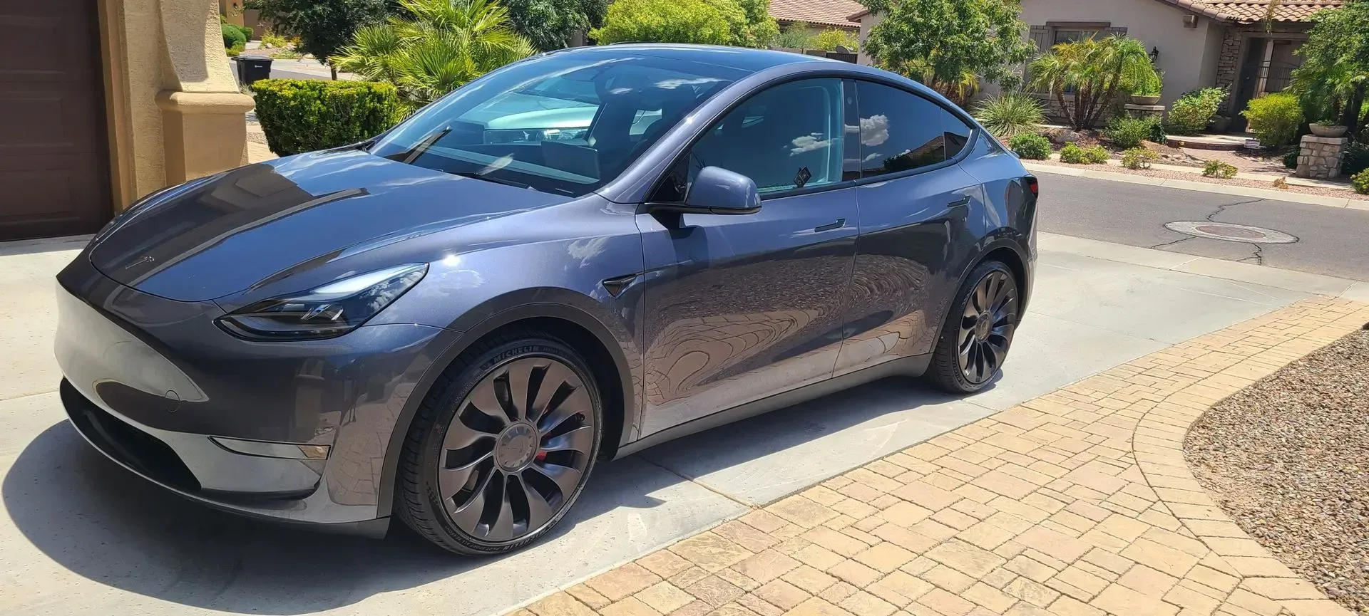 Dark gray Tesla sedan parked on a sunny driveway beside a house