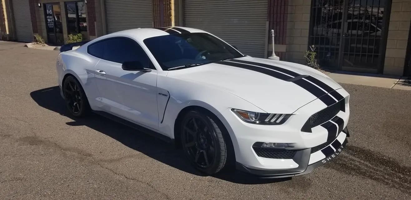 White sports car with black racing stripes parked on a street outside storefronts
