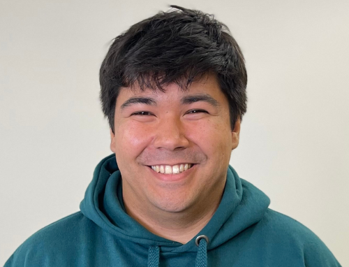 A man wearing a green hoodie is smiling for the camera.