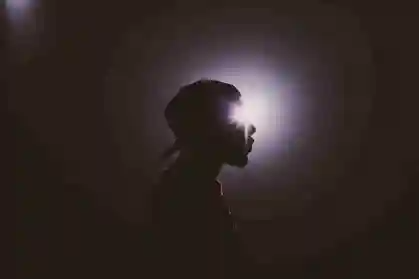 A silhouette of a man in a dark room with a light shining on his face.
