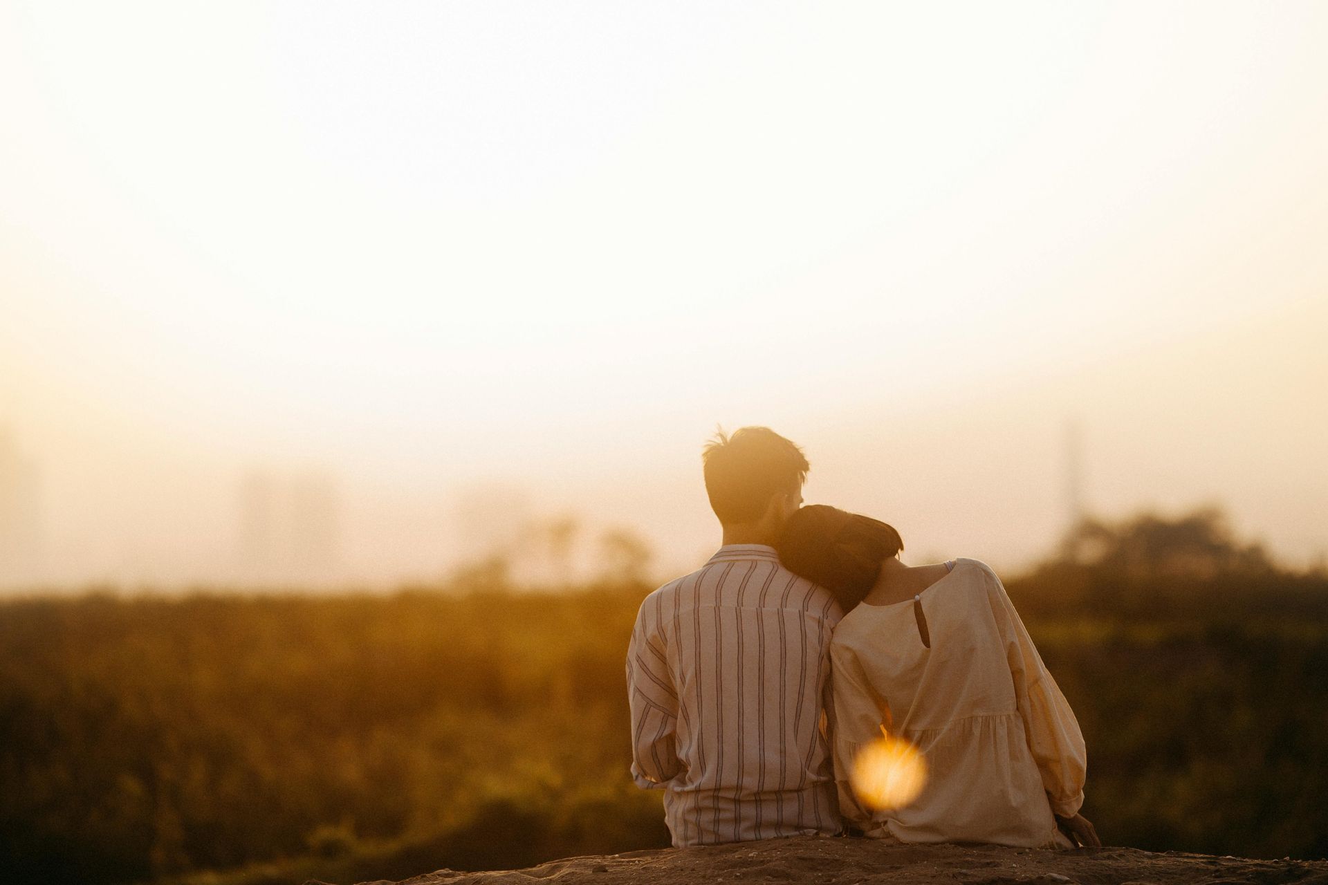 A man and a woman are sitting on top of a hill looking at the sunset.