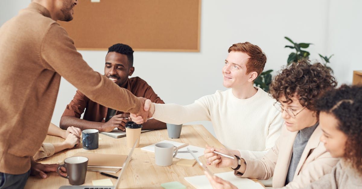A man is shaking hands with a group of people sitting around a table.
