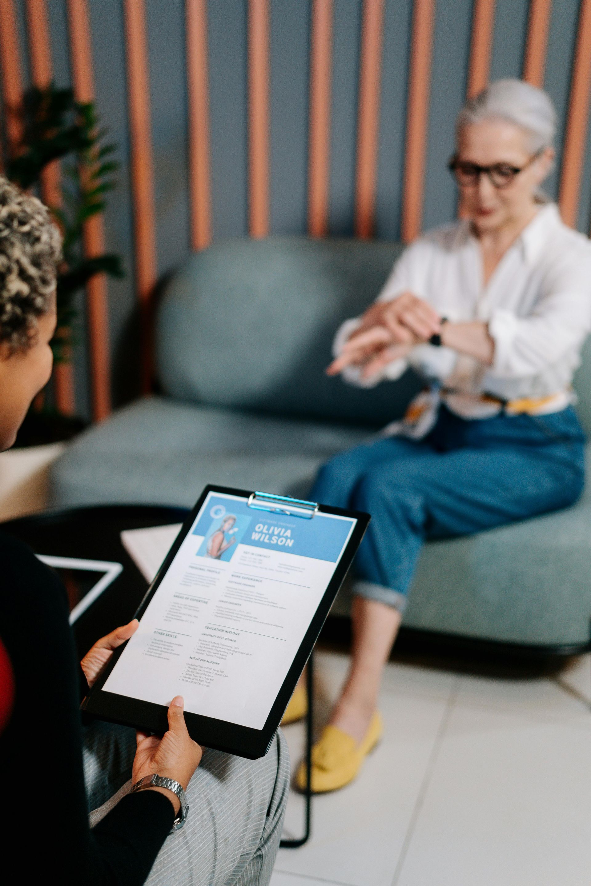 A woman is holding a clipboard with a resume on it in front of an older woman.
