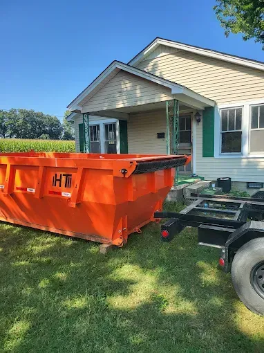 Orange dumpster on a trailer parked beside a house on a sunny lawn
