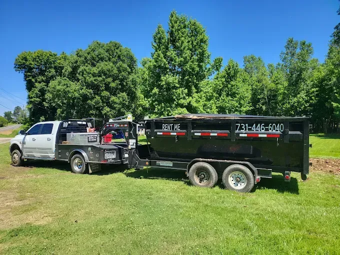 White pickup truck towing a black dump trailer on a grassy lawn under a blue sky