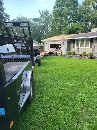 Black trailer and white pickup in a green yard outside a beige house with a garage.