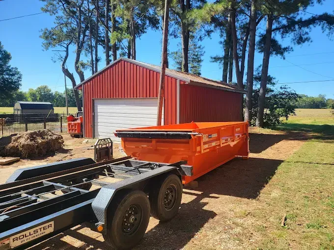 Orange dumpster trailer beside a red barn on a sunny rural property