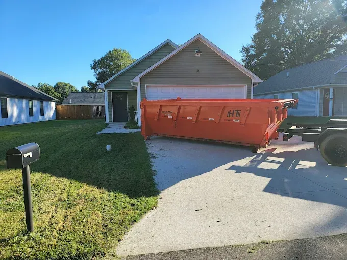 Large orange dumpster in a driveway in front of a beige house on a sunny day