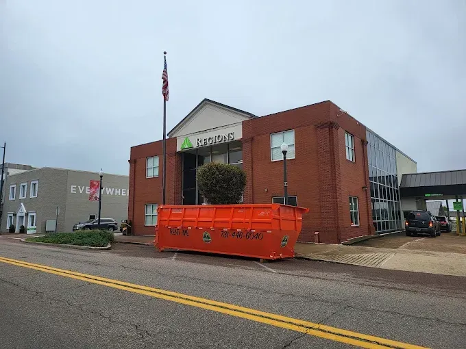 Brick municipal building with flagpole and orange dumpster on the street