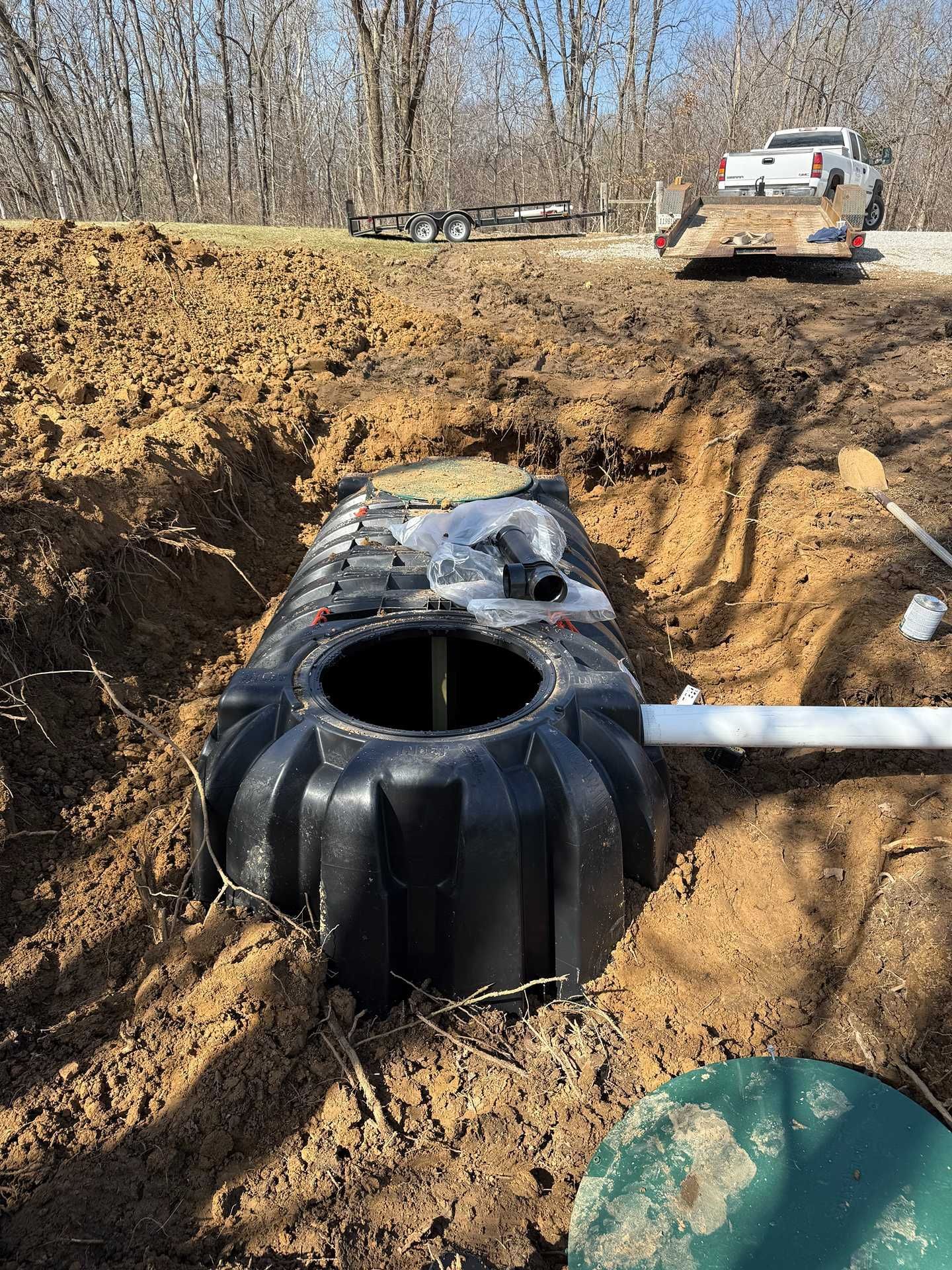 Black water tank installed in a muddy excavation site with a work truck in the background.