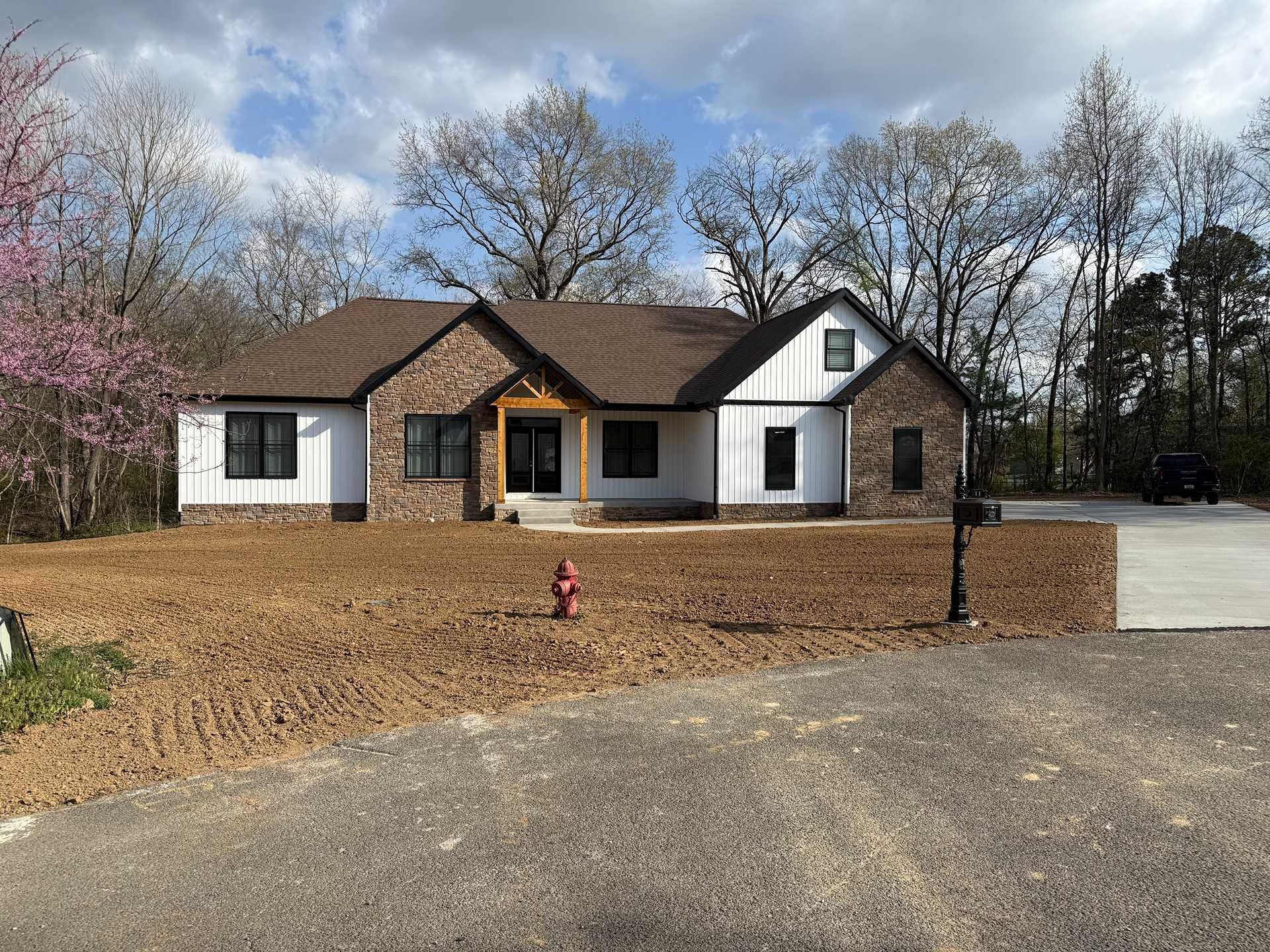 Single-story house with a brown roof, white siding, and a gravel driveway under cloudy skies.