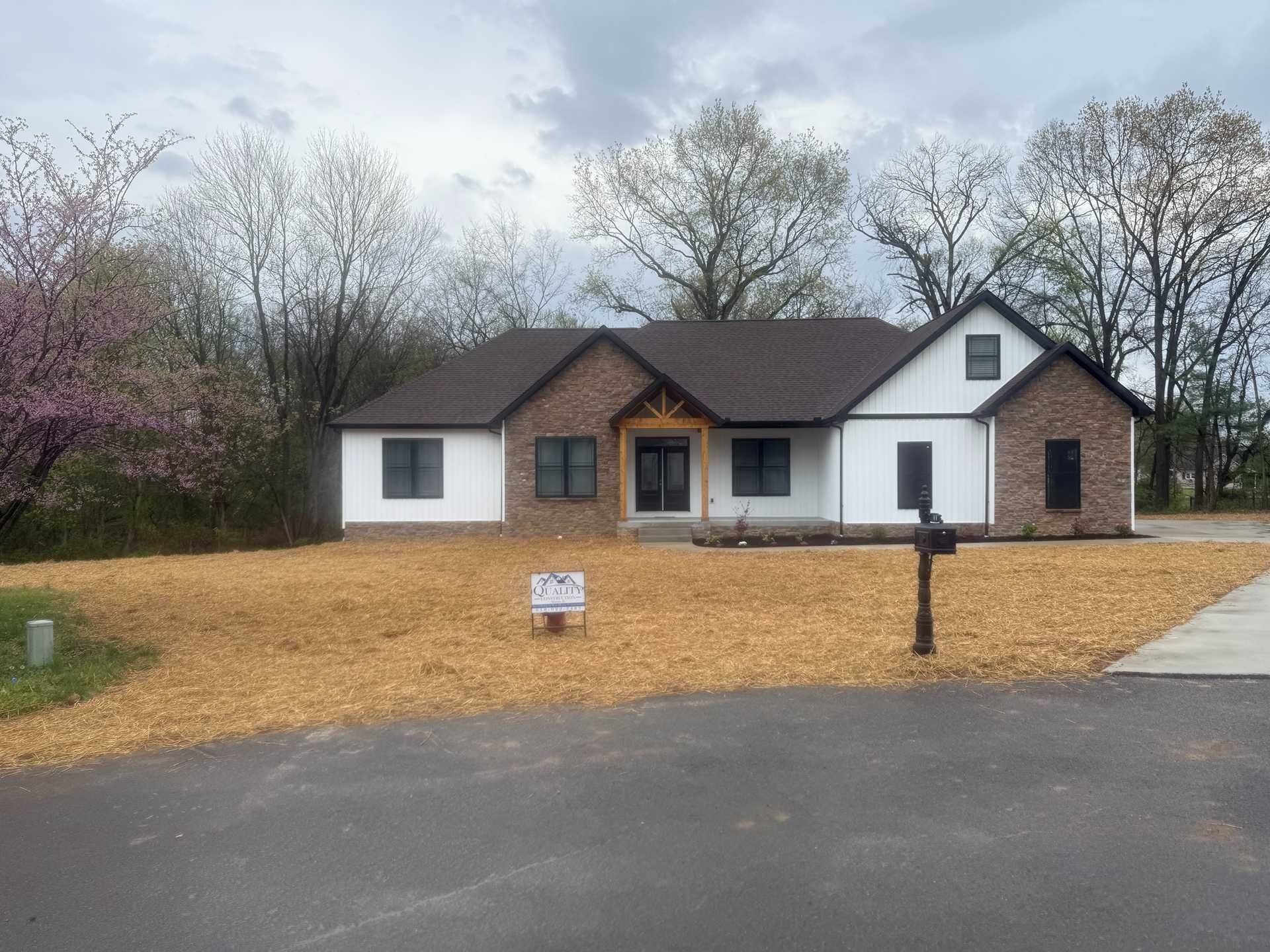 Single-story house with white siding and brick, surrounded by leafless trees and a large gravel yard.
