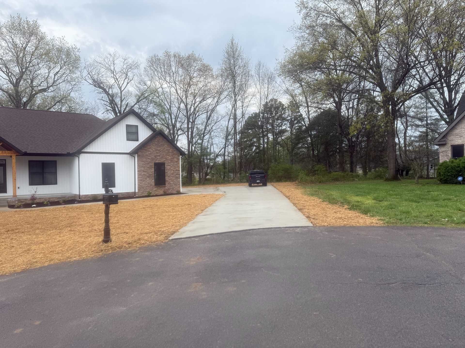 Suburban driveway leading to a house with a gravel parking area and trees under a cloudy sky