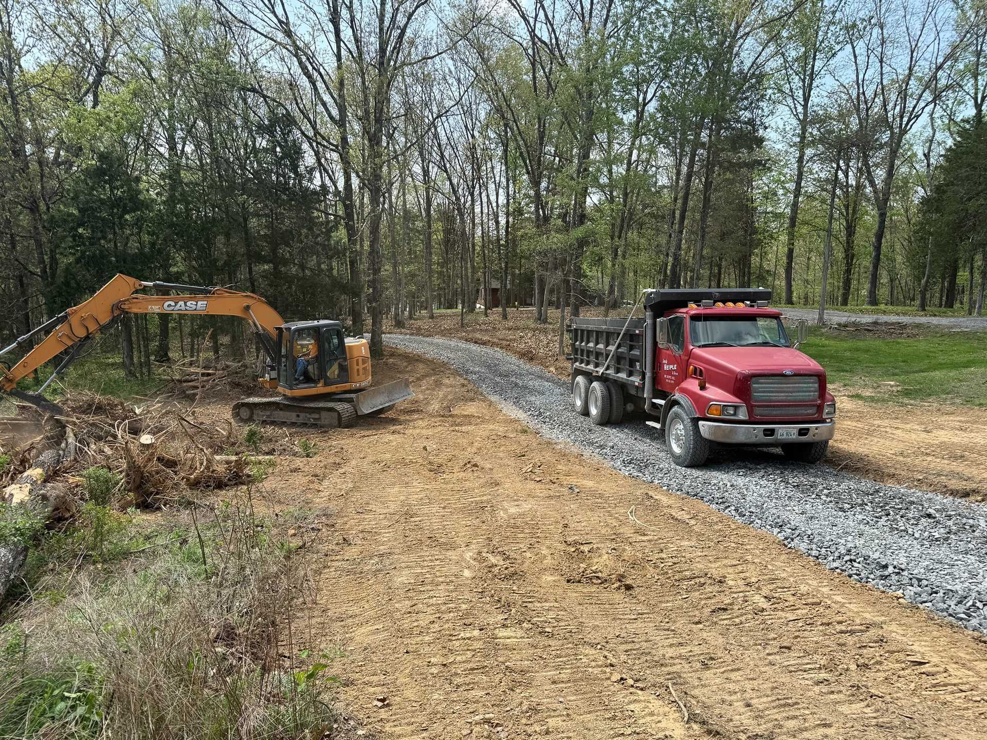 Red dump truck and excavator working on a gravel road in a wooded area