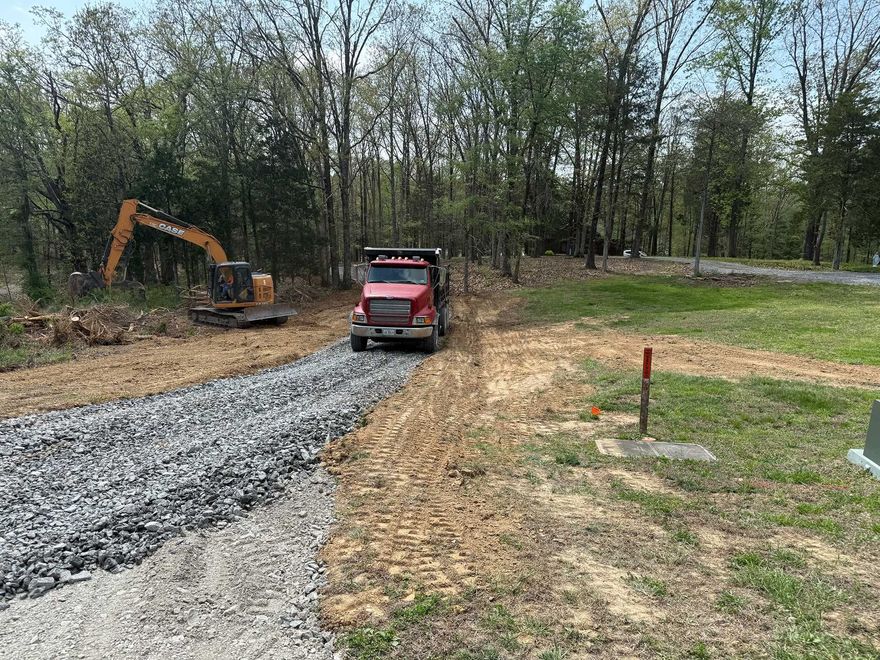 Excavator and red truck on a gravel road in a wooded construction site