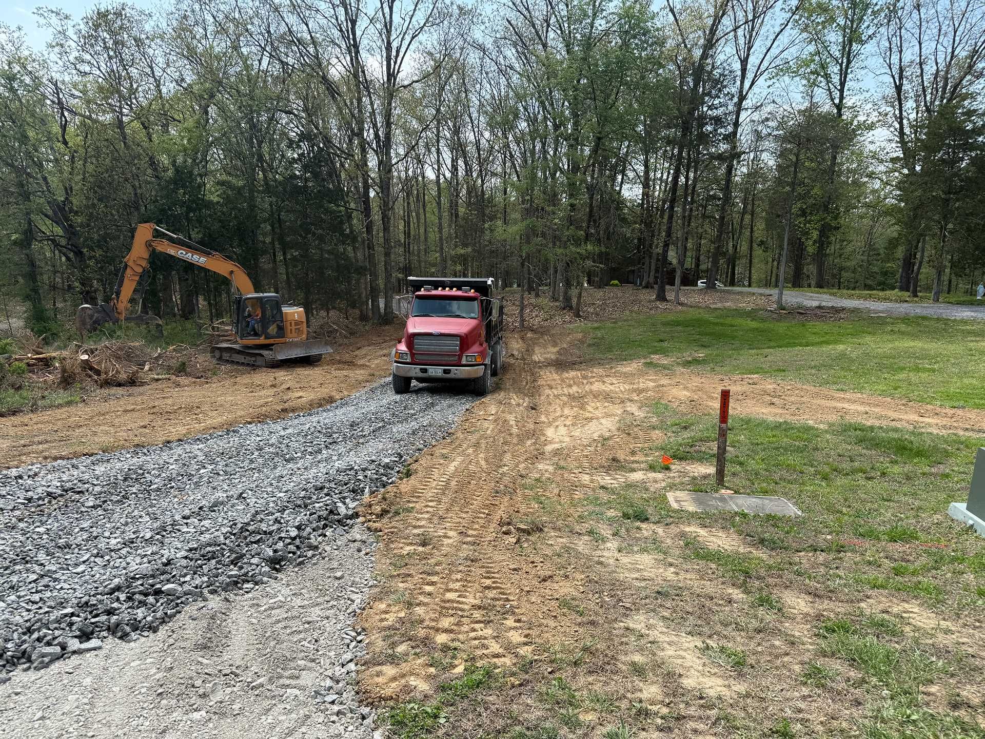 Red dump truck on a gravel road beside an excavator in a wooded construction area