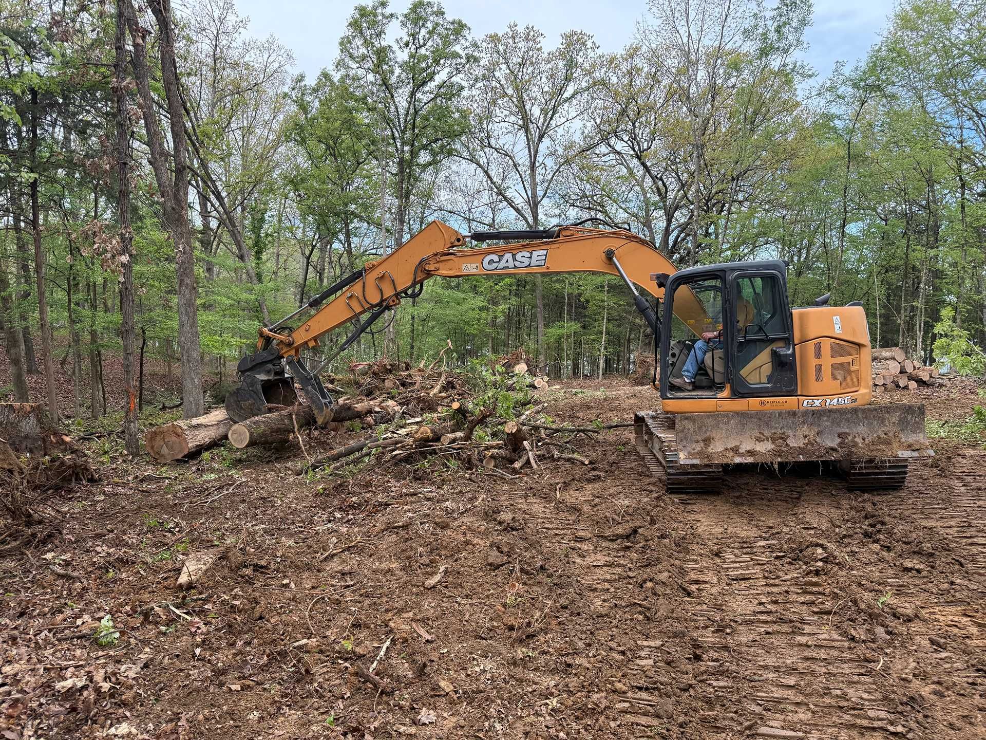 Orange excavator clearing brush in a wooded area