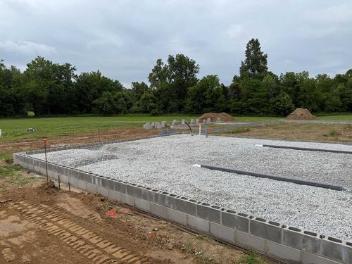 Concrete foundation under construction on a wooded lot with gravel and cinder blocks