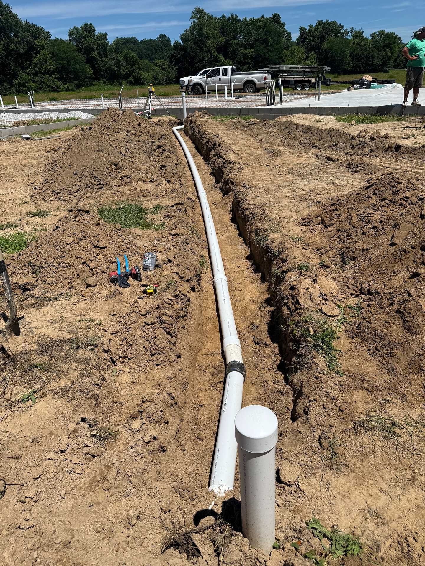 PVC pipe laid in a trench at a construction site with dirt, trucks, and workers in the background
