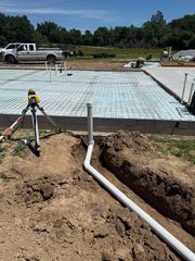 Construction site with concrete slab foundation, pipes in foreground, and truck and equipment in the background
