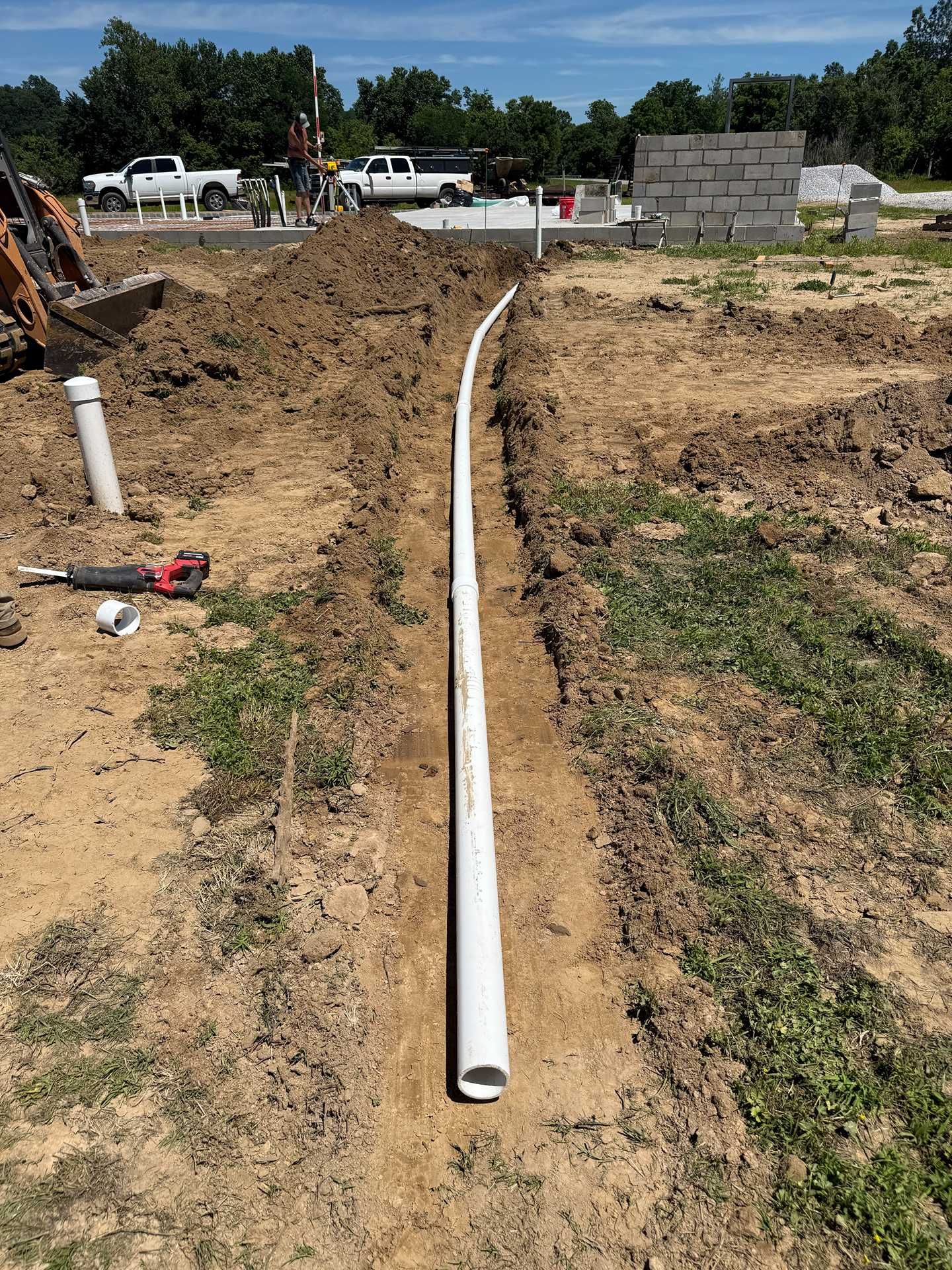 White PVC pipe laid in a dirt trench at a construction site, with building materials in the background