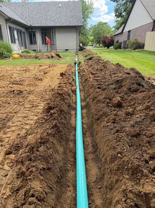 Trenched yard with blue pipe laid between piles of soil beside two houses
