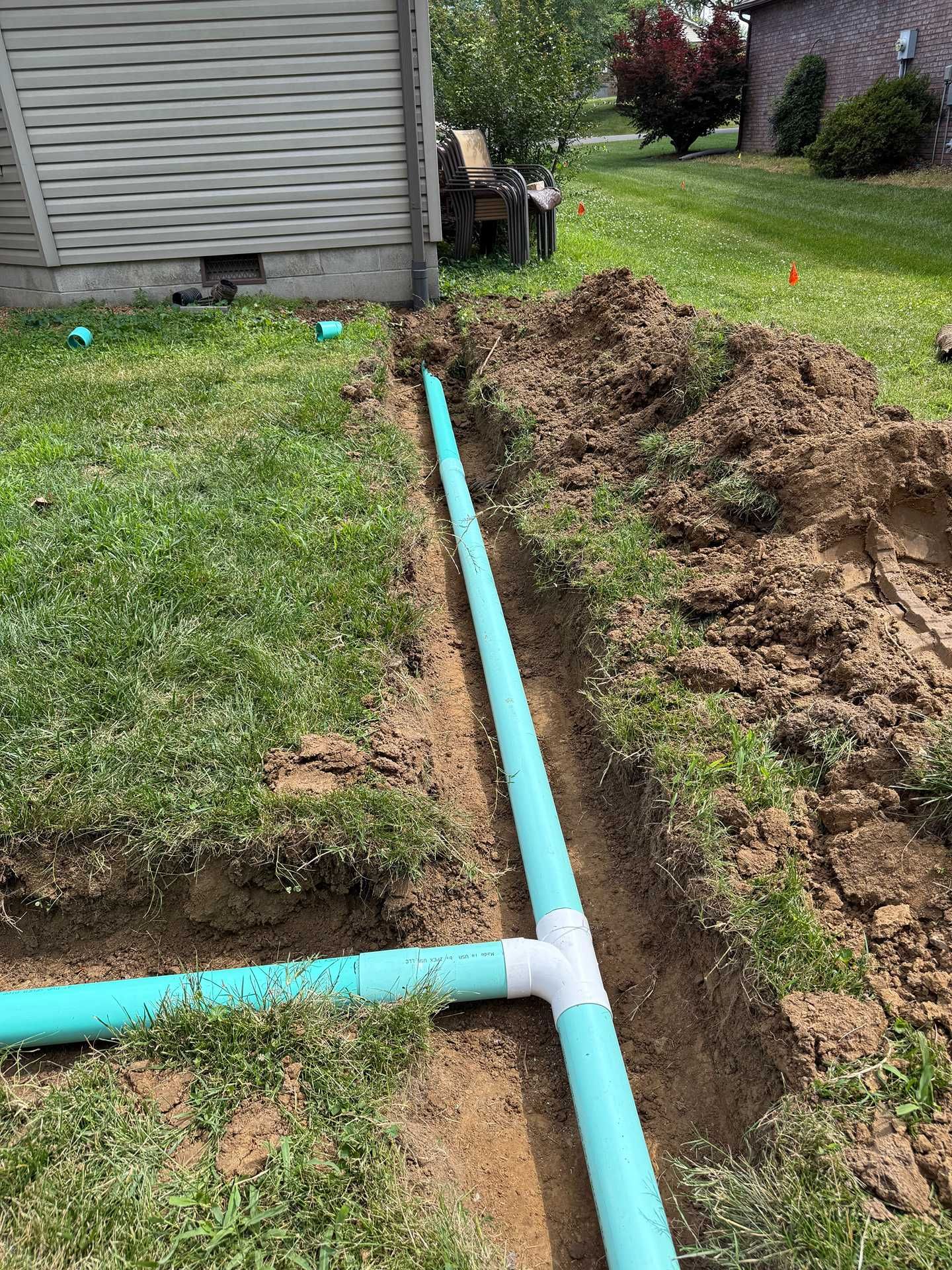 Blue PVC pipes in a trench beside a house, with excavated soil along a grassy yard.