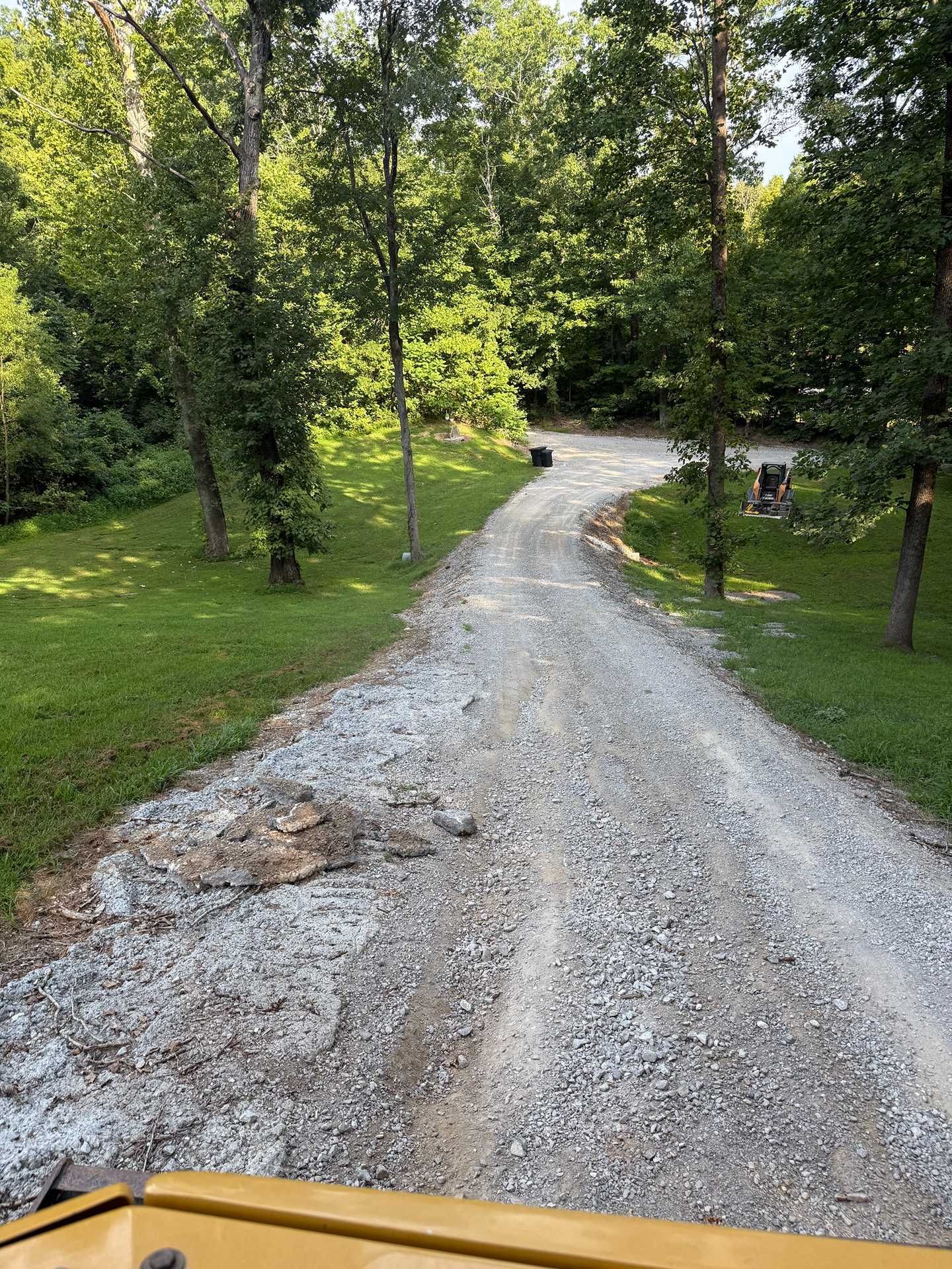 Gravel driveway winding through green trees and grass, viewed from a vehicle