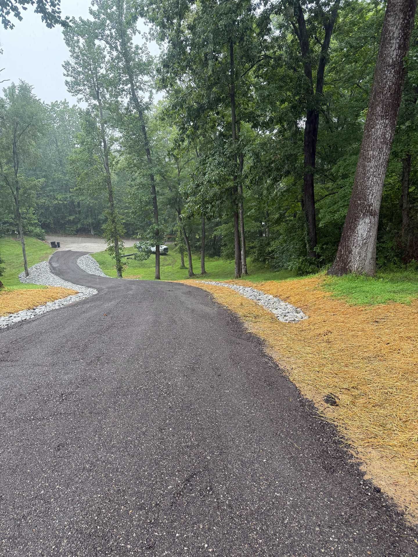 Wet gravel path winding through a wooded park with trees and grass after rain
