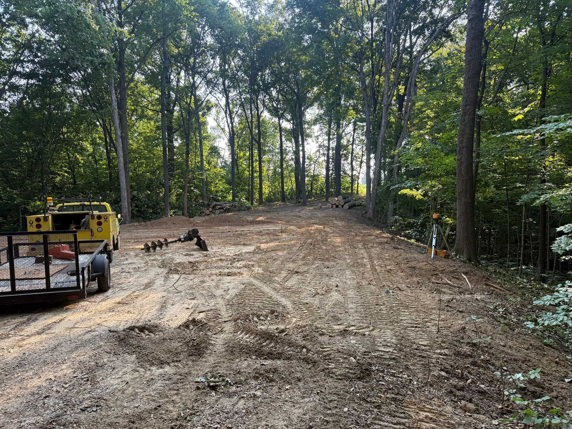 Dirt clearing in a wooded area with heavy equipment on the left and trees surrounding the site