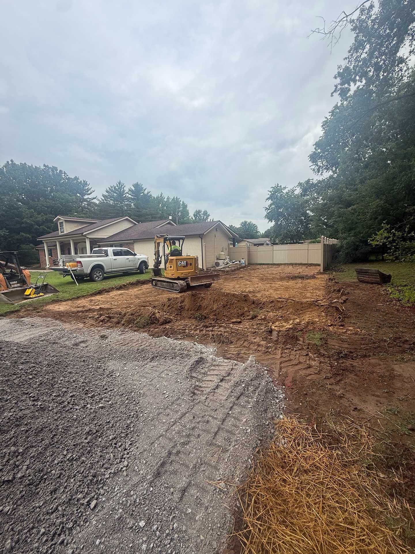 Gravel driveway under construction beside a house, with a white truck and dirt piled along the right side.