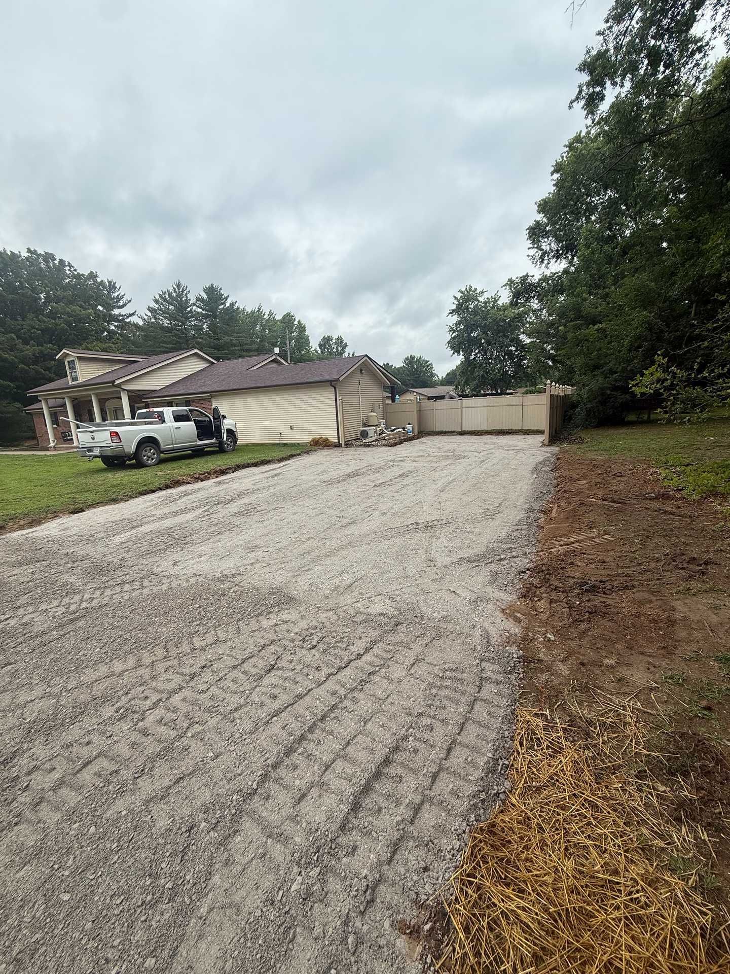 Gravel driveway leading to a beige house with a white truck and overcast sky